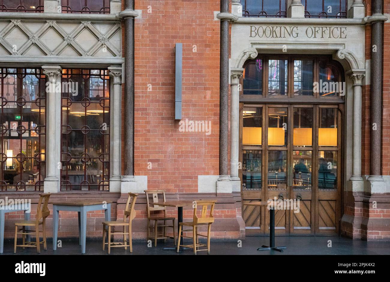 Die Außenfassade und die Tür zum Buchungsbüro Restaurant in St. Pancras Station mit ein paar leeren Tischen und Stühlen. Stockfoto