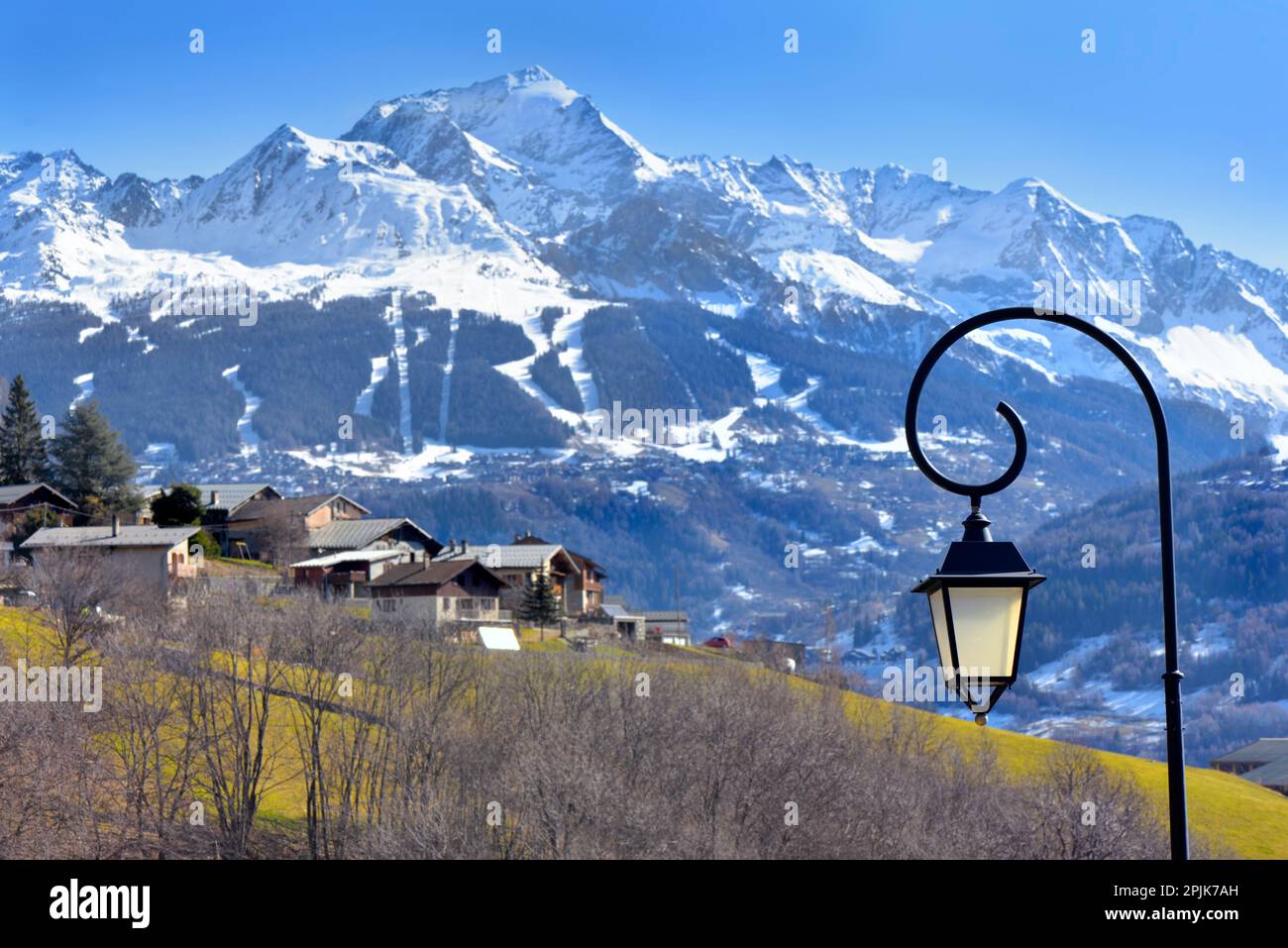 Alte Straßenlampe eines alpinen Dorfes mit weißer, aufsteigender Landschaft im Hintergrund Stockfoto