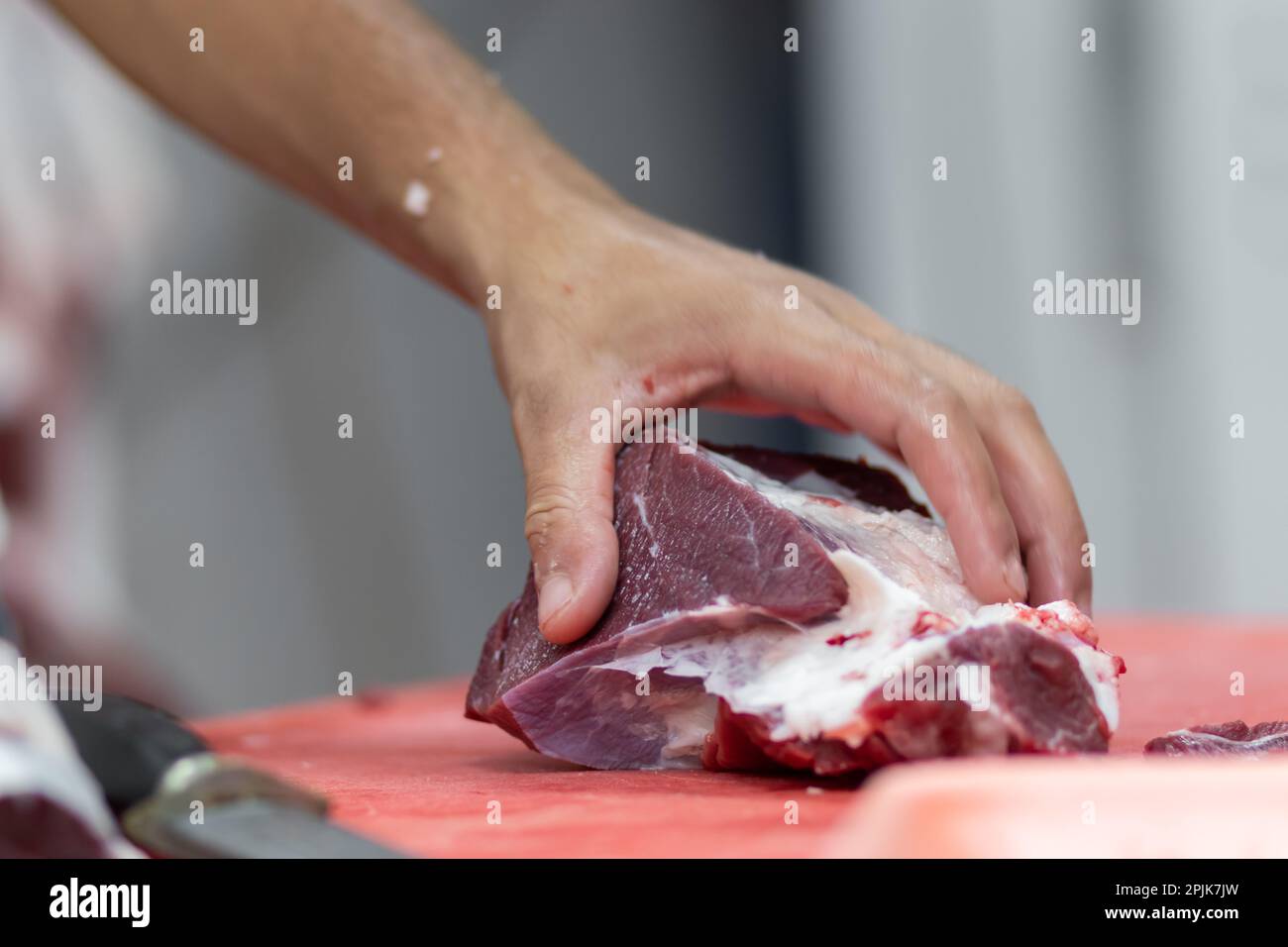 Ein Metzger schneidet frisches Rindfleisch mit einem scharfen Messer in Stücke. Unscharfer Hintergrund Stockfoto