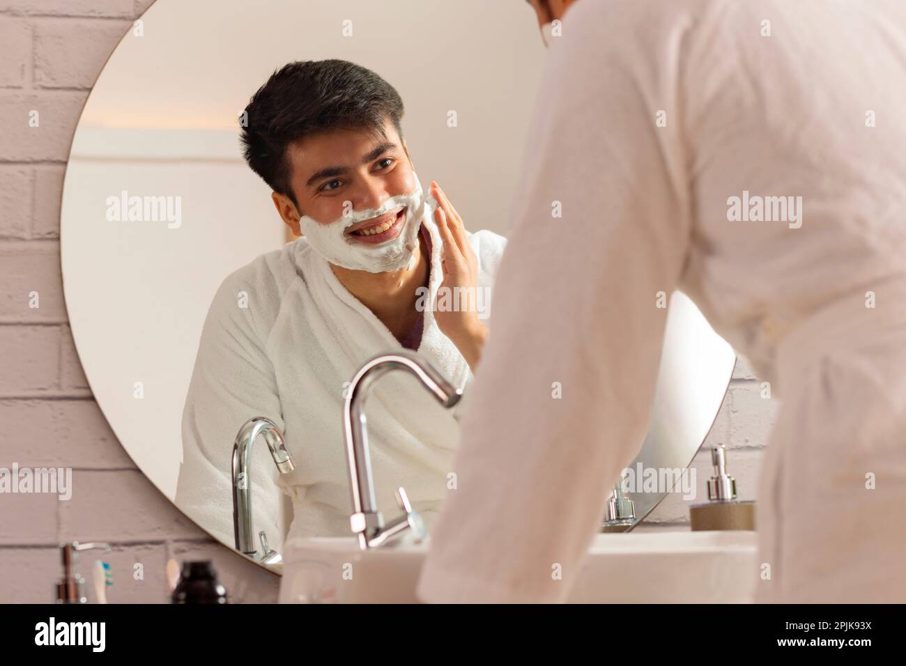 Junger Mann, der sich in einem Badezimmer zu Hause Rasiercreme ins Gesicht aufträgt Stockfoto