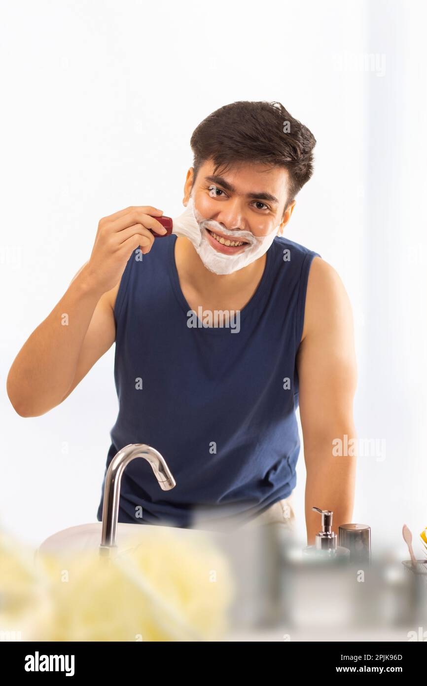 Junger Mann, der sich zu Hause im Badezimmer Rasiercreme ins Gesicht aufträgt Stockfoto