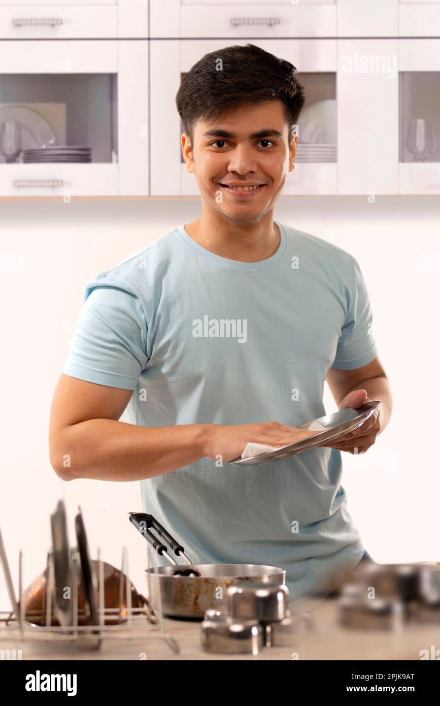 Junger Mann, der nach der Reinigung in der Küche einen Teller abwischt Stockfoto
