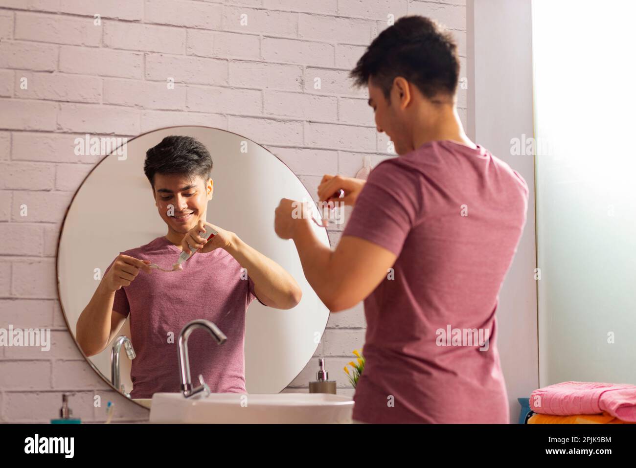 Ein junger Mann, der Zahnpasta auf einer Zahnbürste ausdrückt Stockfoto