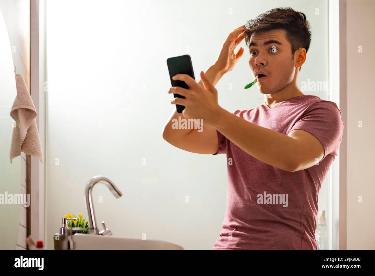 Junger Mann mit Handy beim Zähneputzen im Badezimmer Stockfoto