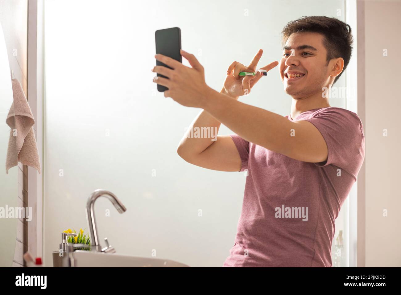 Junger Mann, der beim Videogespräch Gesten macht, während er im Badezimmer Zähne putzt Stockfoto