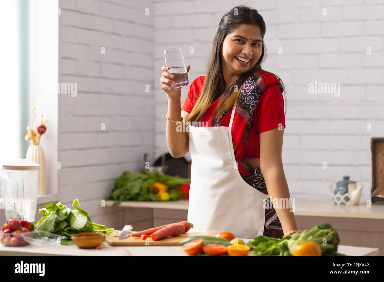 Frau trinkt Wasser, während sie Gemüse in der Küche hackt Stockfoto