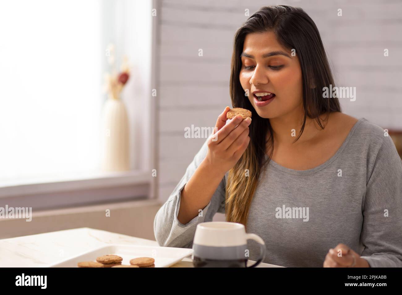 Eine Frau, die zu Hause Kekse mit Tee isst Stockfoto