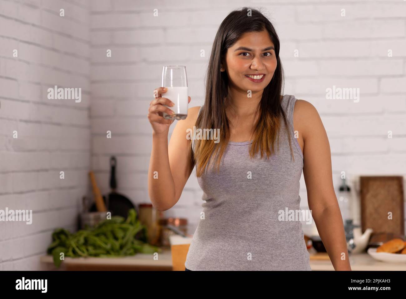 Fröhliche Frau, die ein Glas Milch in der Küche hält Stockfoto