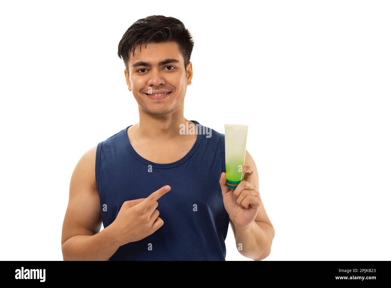 Fröhlicher junger Mann, der auf eine Gesichtswaschung zeigt, die er in der Hand hält, vor weißem Hintergrund Stockfoto