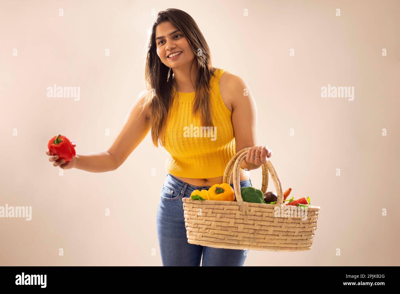 Lächelnde Frau mit einem Korb aus frischem Gemüse und roter Paprika vor weißem Hintergrund Stockfoto