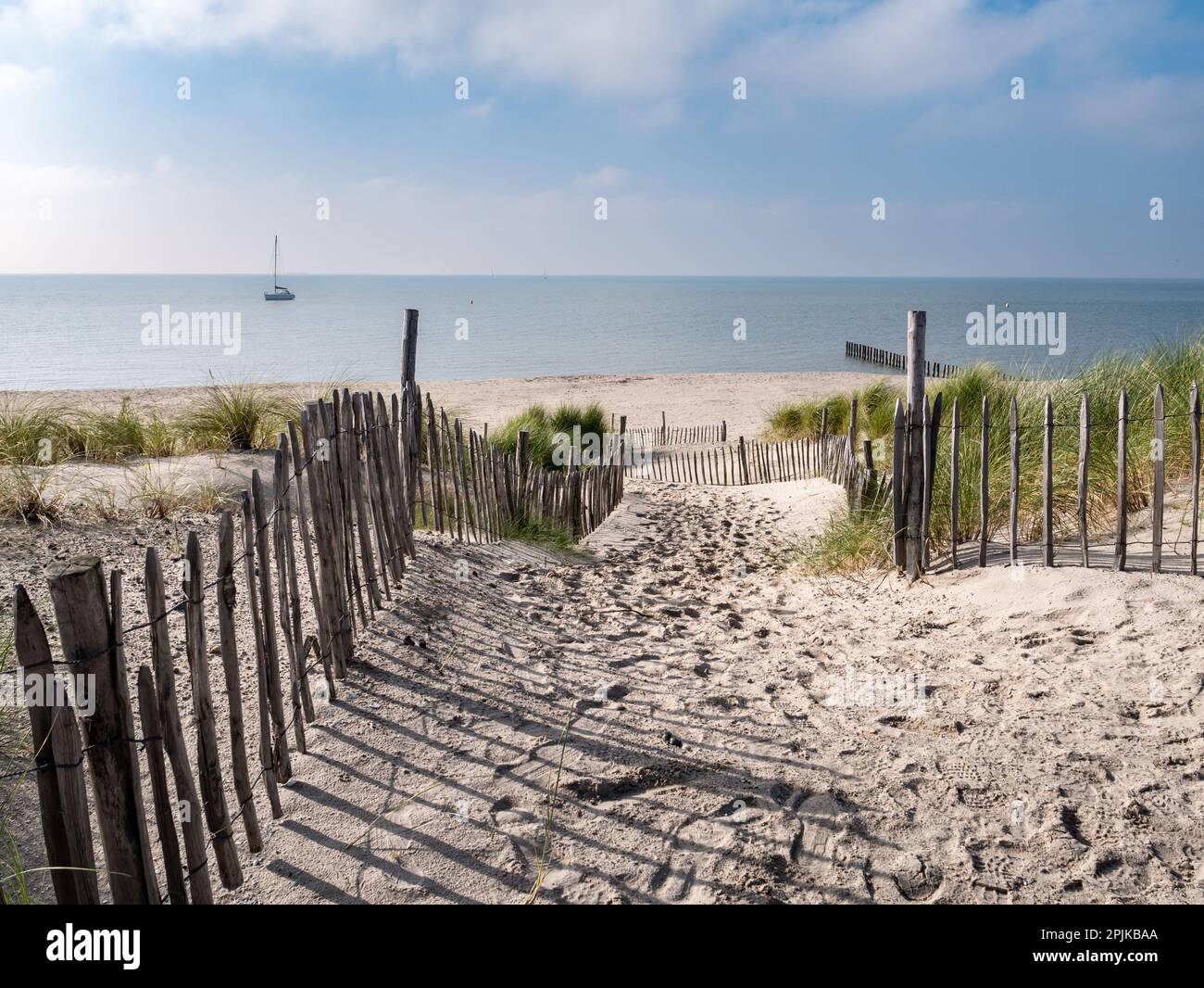 Fußweg in Sanddünen zum Strand der Insel Marker Wadden und Segelboot auf dem See Markermeer, Niederlande Stockfoto