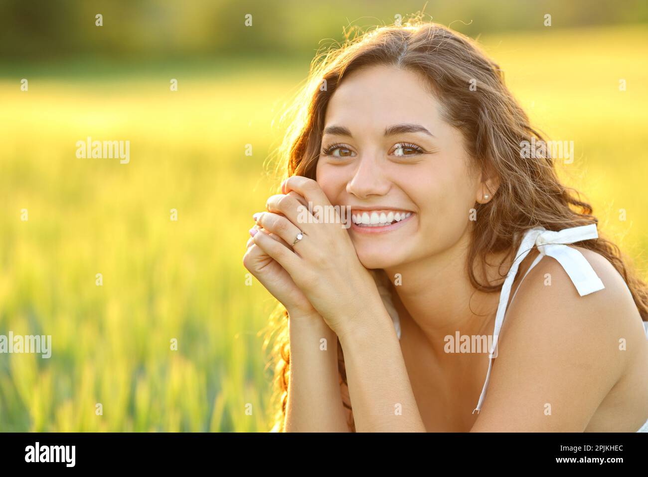 Glückliche Frau, die auf einem Feld posiert und bei Sonnenuntergang in die Kamera schaut Stockfoto