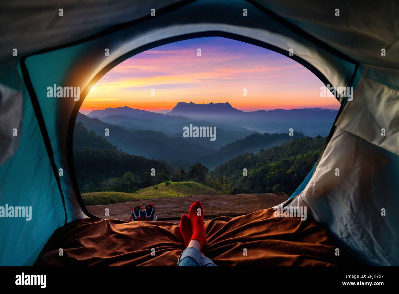 Frau überquert Bein auf Decke im Campingzelt mit Schlafsäcken auf Bergsteigen. Blick von innen auf die Berge von Doi luang chiang dao. Stockfoto