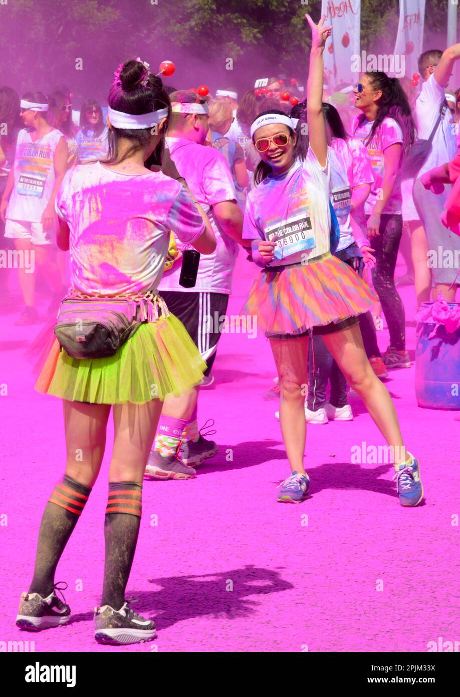 Läufer posieren beim Colour Run UK in Birmingham, tragen Tutus und sind mit Farbpulver bedeckt, während andere Läufer im Hintergrund sichtbar sind Stockfoto