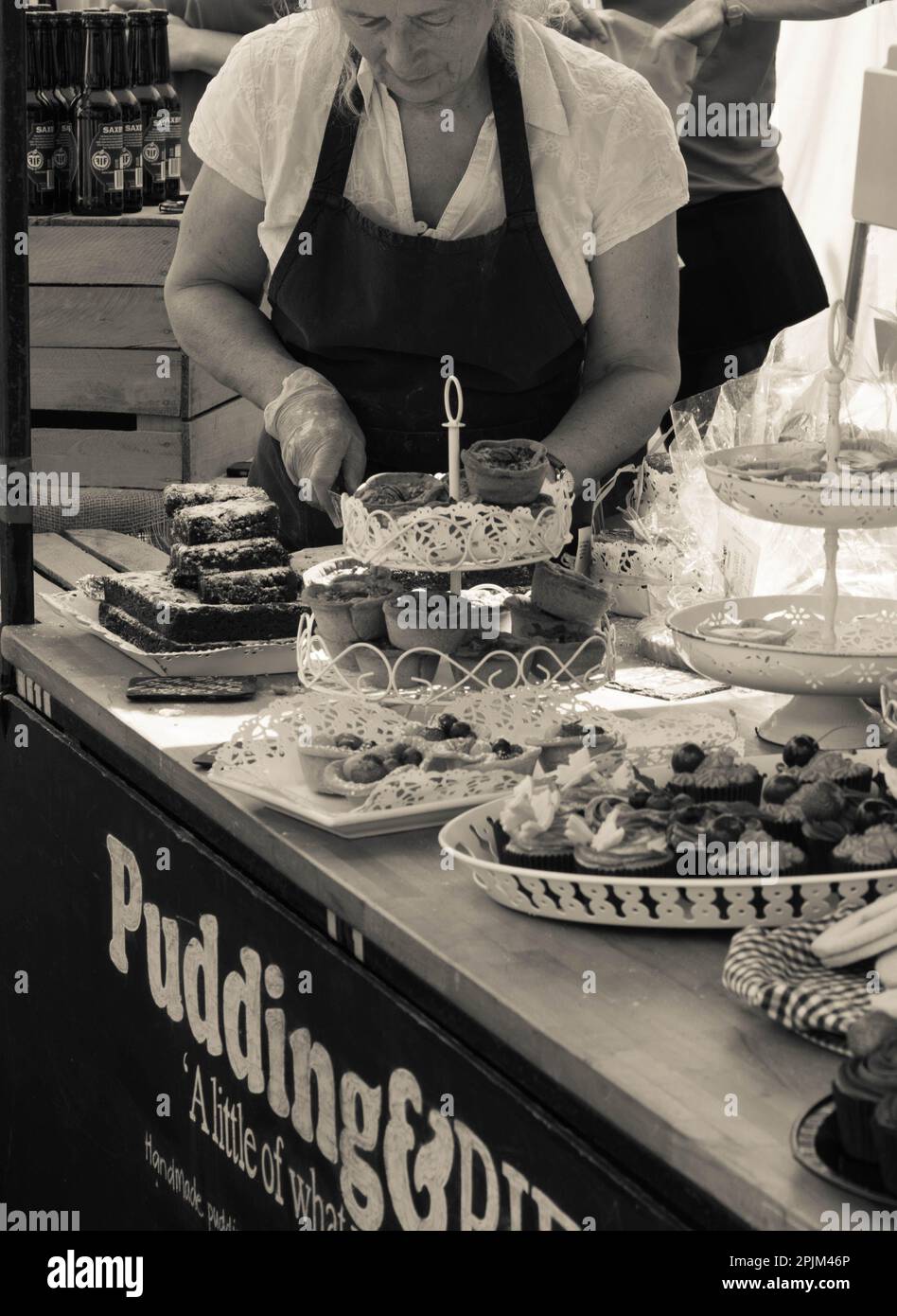 Bild in Sepia-Farbtönen: Imbissstand am Oundle Market in Northamptonshire, England, Großbritannien, mit dem Besitzer des Imbissbuches, der Kuchen schneidet Stockfoto