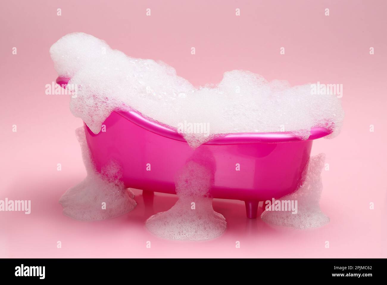 Spielzeugbadewanne mit Schaumstoff auf pinkfarbenem Hintergrund Stockfoto