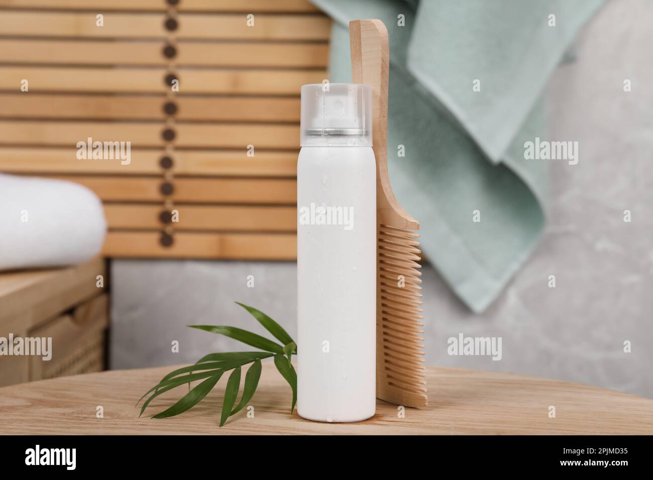 Trockenes Shampoo-Spray, grüne Blätter und Kamm auf Holztisch im Badezimmer Stockfoto