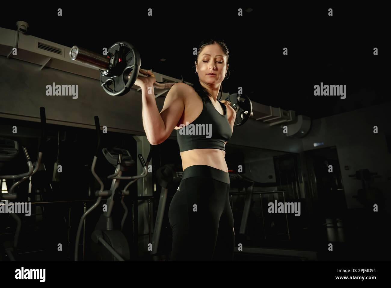 Fitness-Frau, die mit schweren Scheiben Barbell-Squats macht. Barbell auf den Schultern hinter dem Rücken des Mädchens Stockfoto