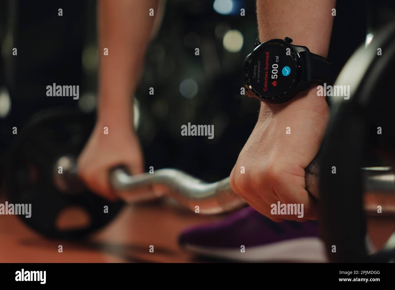 Nahaufnahme einer Smartwatch an der Hand einer Frau, die im Fitnessstudio auf dunklem Hintergrund eine schwere Klingel hebt. Kalorienverbrennung. Technologie und Sportkonzept Stockfoto