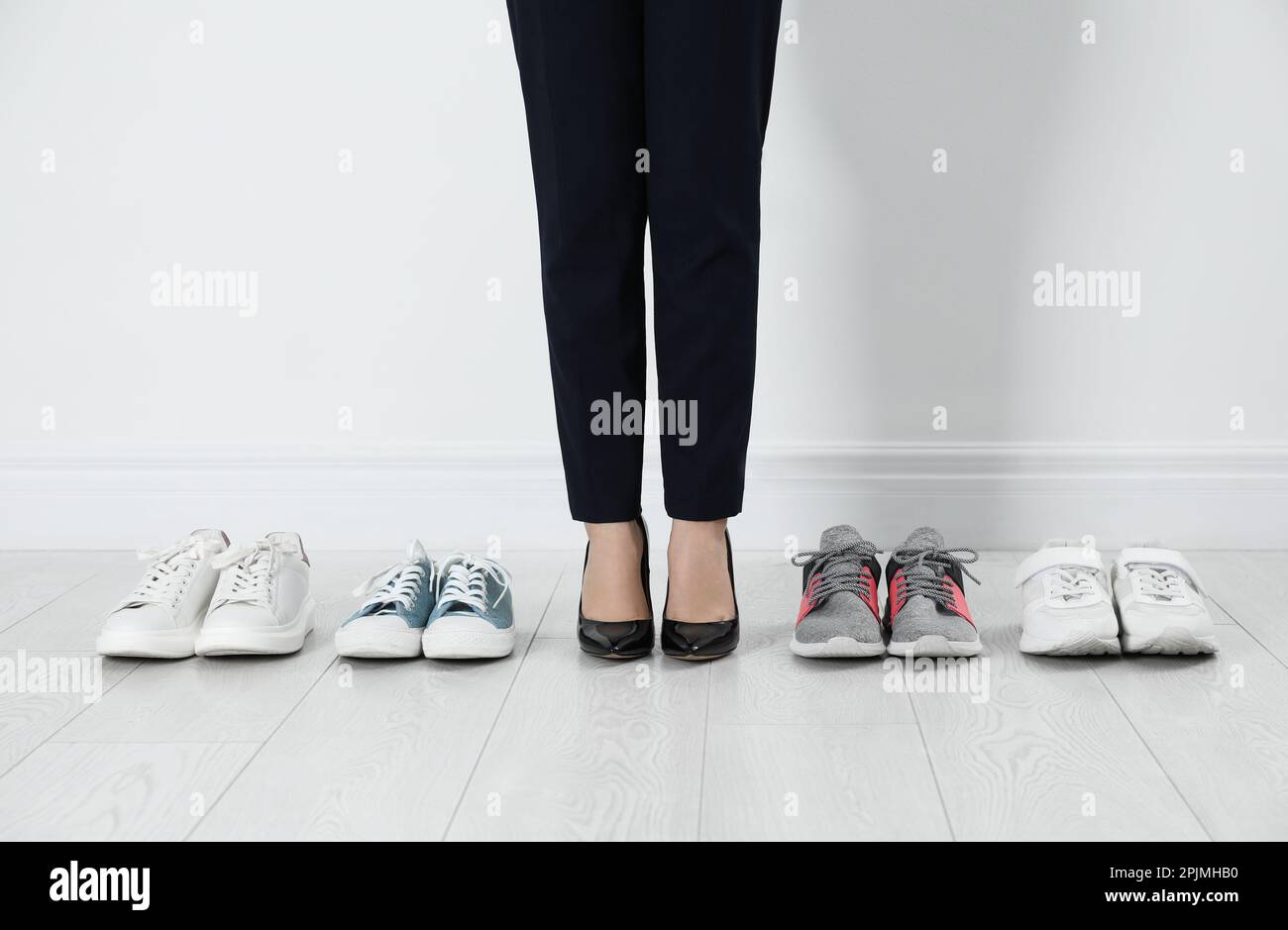 Verschiedene bequeme Sneaker in der Nähe von Geschäftsfrau, die Schuhe mit hohem Absatz drinnen und Nahaufnahme trägt Stockfoto