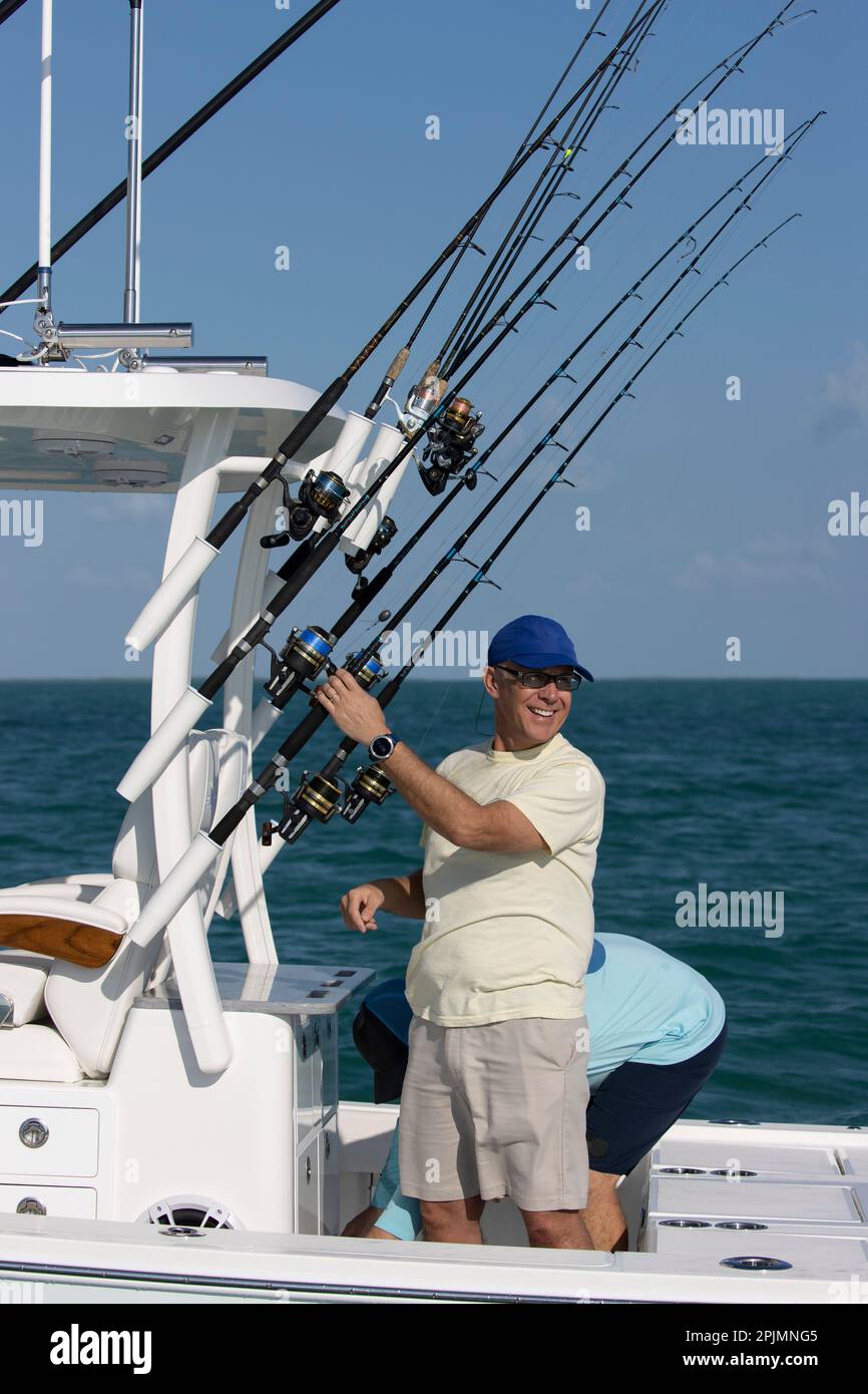 Ein lächelnder Mann, der auf einem Boot steht und Angelruten hält. Stockfoto