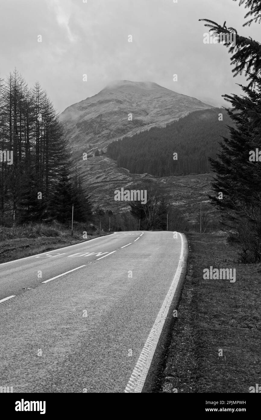 Die Hauptstraße A85 durch das schottische Hochland mit einem wolkenbedeckten Berg im Hintergrund. Stockfoto