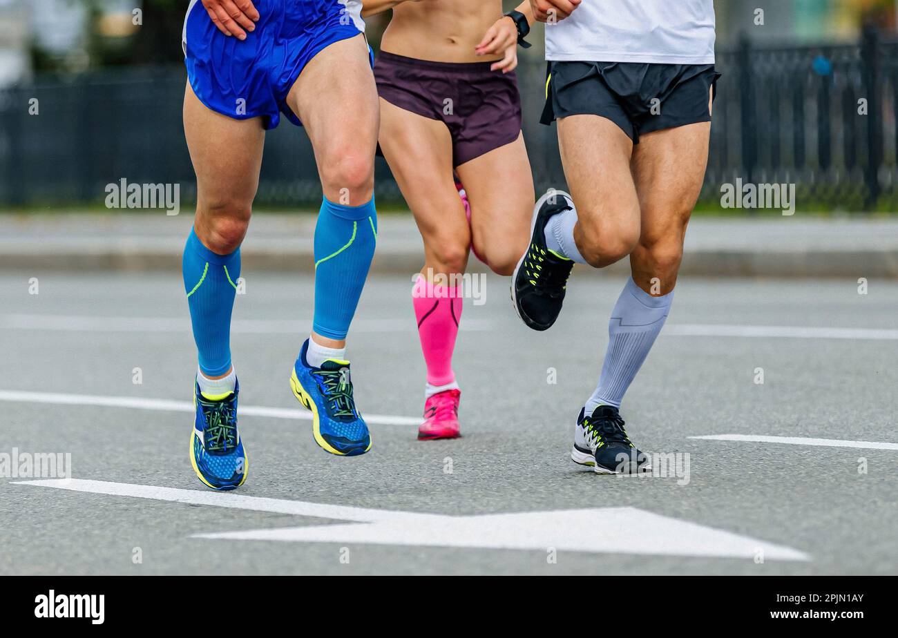 Drei Läufer, männliche und weibliche Athleten, laufen Marathonrennen, Joggingbeine in Kompressionssocken Rennen auf der Straße Stockfoto