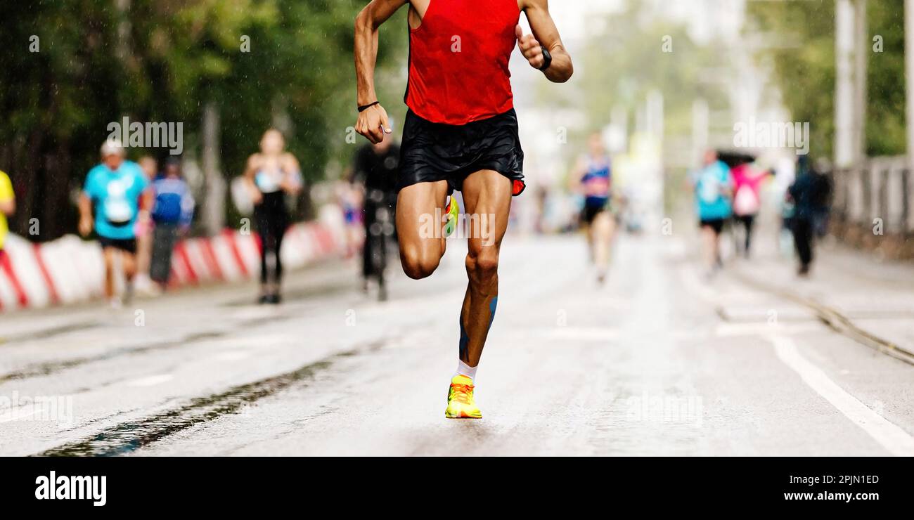 Männlicher Läufer läuft Marathonrennen, joggt nach Regen auf nassem Asphalt, Sommersportspiele Stockfoto