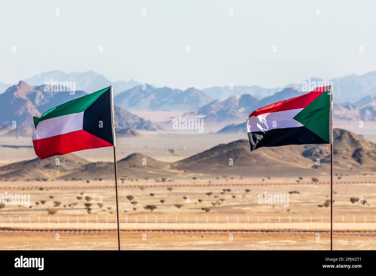 Kuwaitische und sudanesische Flaggen, die sich im Wind versammeln, in der saudiarabischen Wüste mit Bergen im Hintergrund, Al Ula, Saudi-Arabien Stockfoto