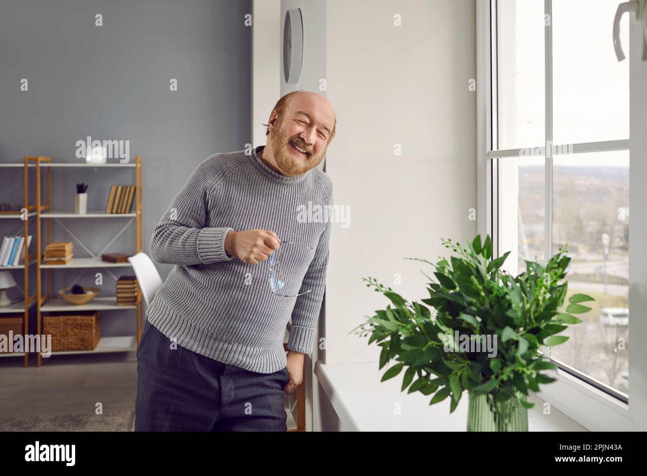 Glücklicher lächelnder Senior Mann, der zu Hause am Fenster stand Stockfoto