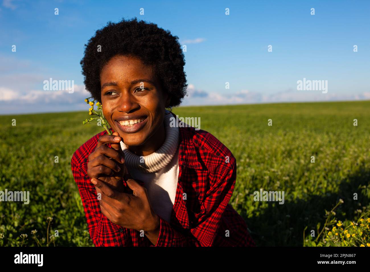 Ein Mann mit langen Haaren auf grüner Wiese, der Sonne und blauen Himmel mit Wolken genießt Stockfoto