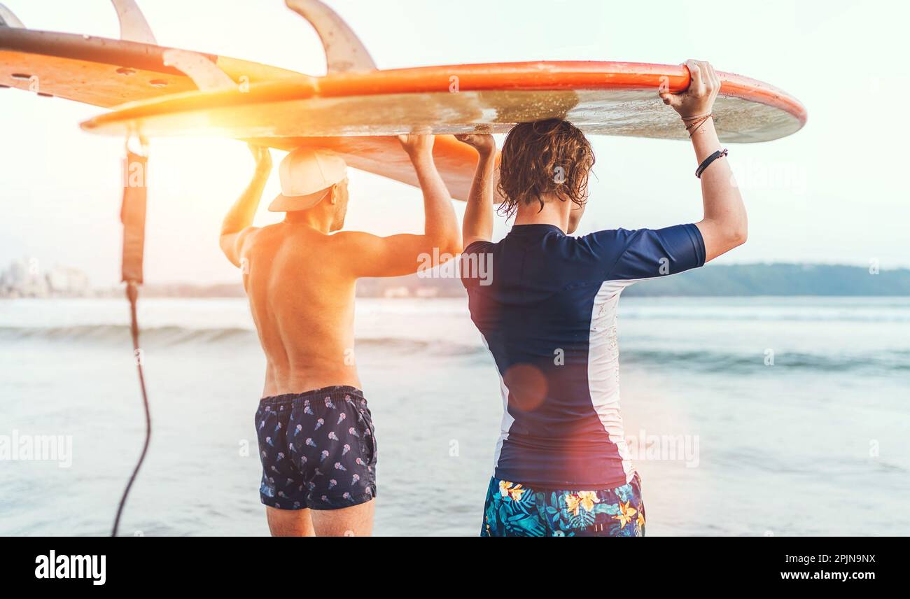 Teenager-Junge mit seinem Vater mit Surfbrettern auf den Köpfen, die in den Wellen am Strand von Udawalawe in Sri Lanka spazieren. Familien-Aktivurlaub oder sportlich aktiv pe Stockfoto