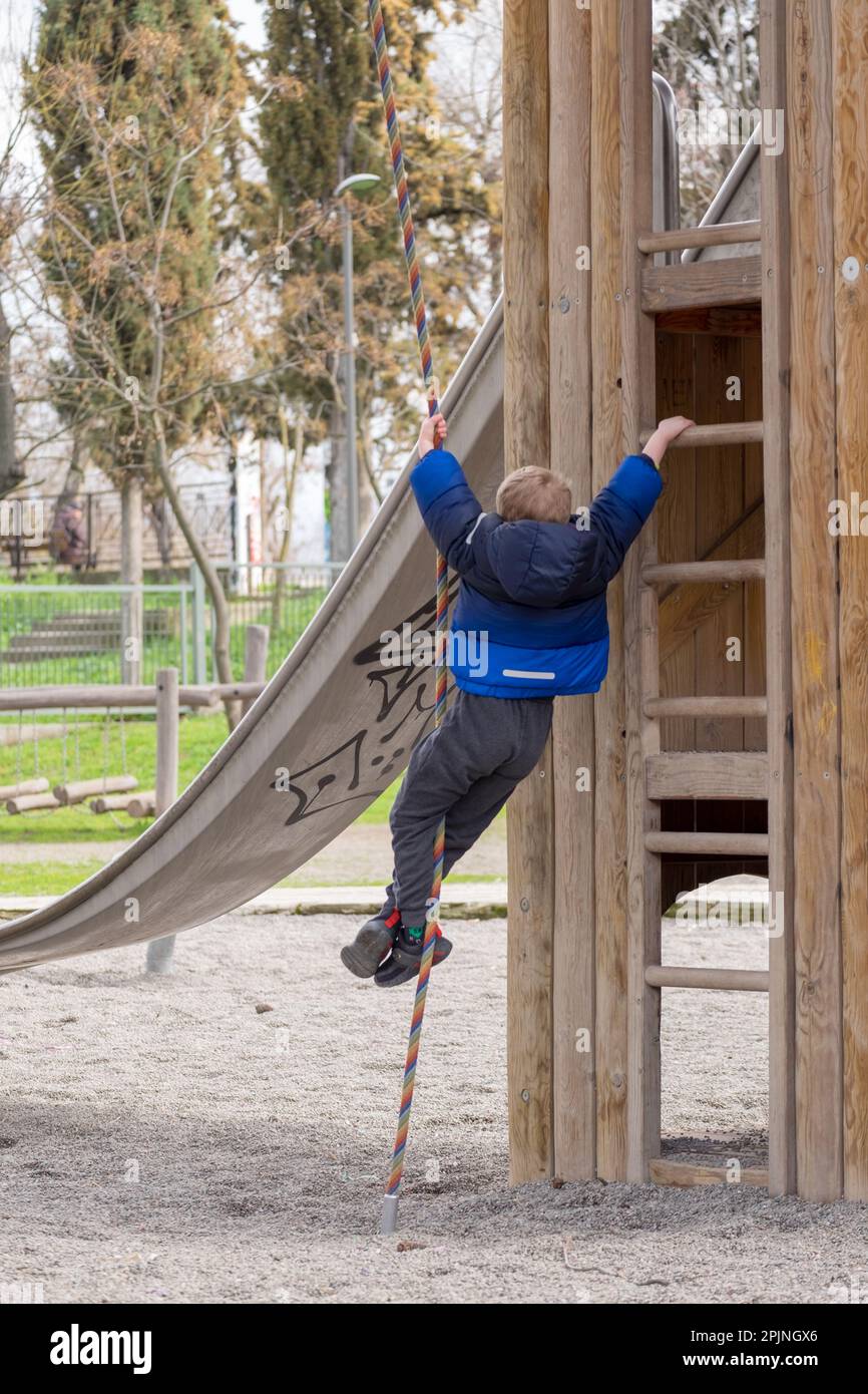 Süßer kleiner Junge mit blonden Haaren, klettert an einem Seil auf dem Spielplatz Stockfoto