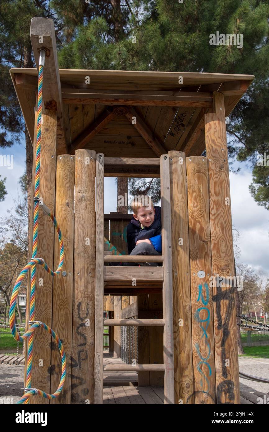 Süßer kleiner Junge, der Verstecken spielt und sich in einem Holzturm auf dem Spielplatz versteckt Stockfoto