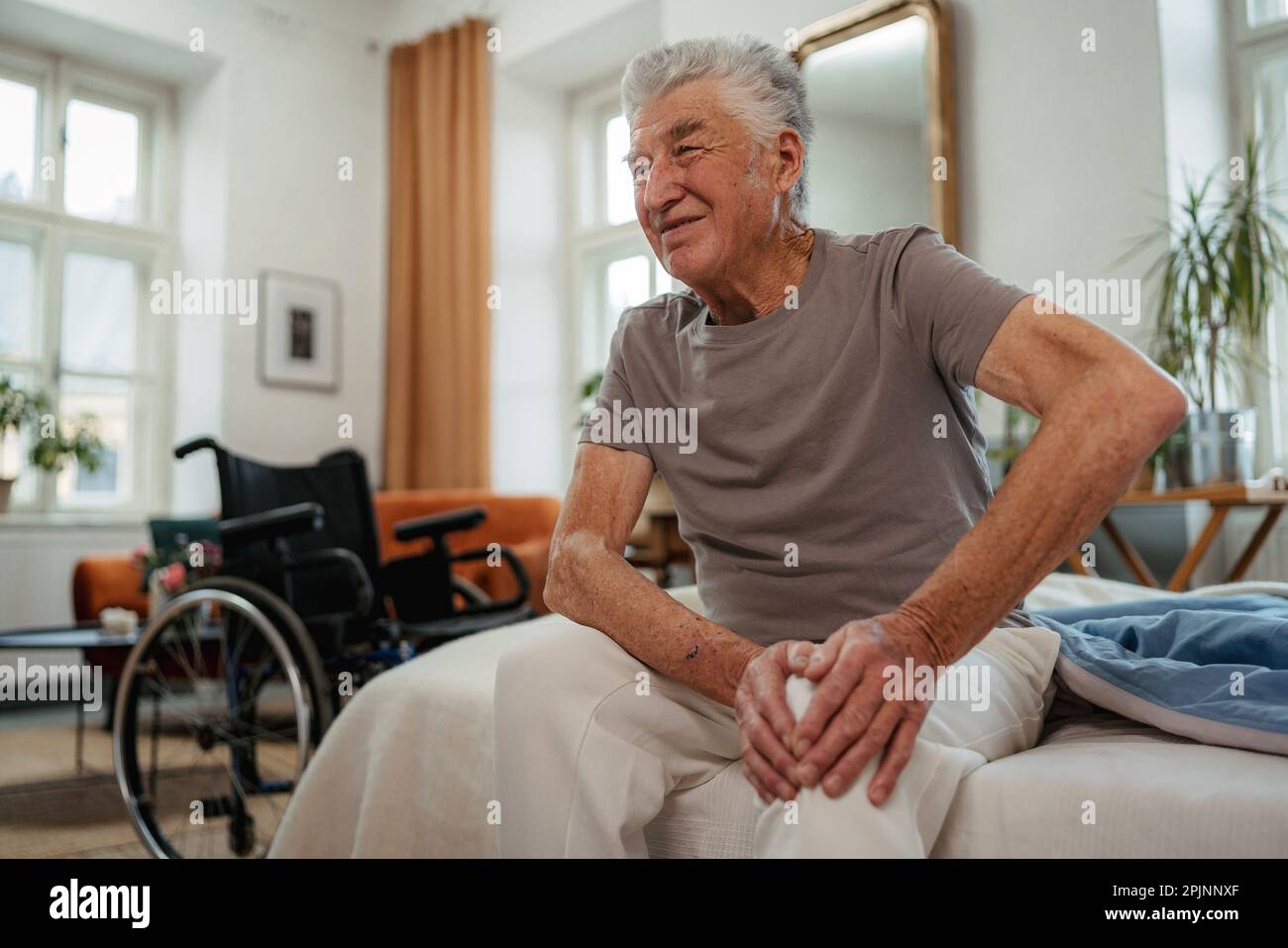 Porträt eines Seniorenmannes mit Knieschmerz, der auf einem Bett sitzt. Stockfoto