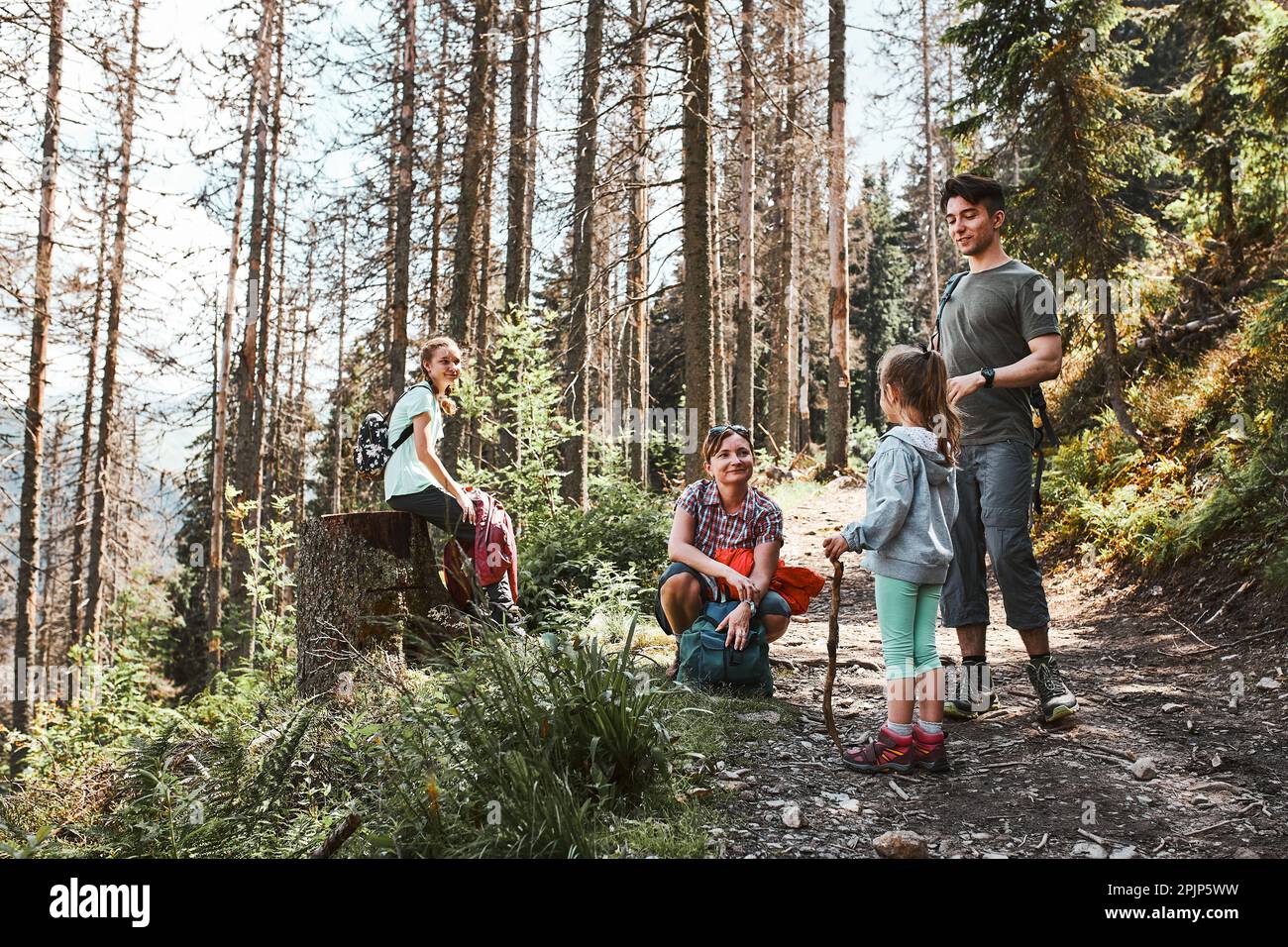 Familie mit Rucksäcken wandern in den Bergen aktiv Sommerurlaub zusammen verbringen Wandern auf Waldweg, reden und bewundern Natur Mountain lan Stockfoto