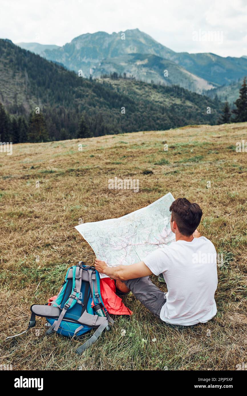 Die Familie untersucht eine Karte von Bergversuchen, die auf Gras sitzen und den Sommertag während eines Urlaubs in den Bergen genießen. Menschen verbringen aktiv Zeit Stockfoto
