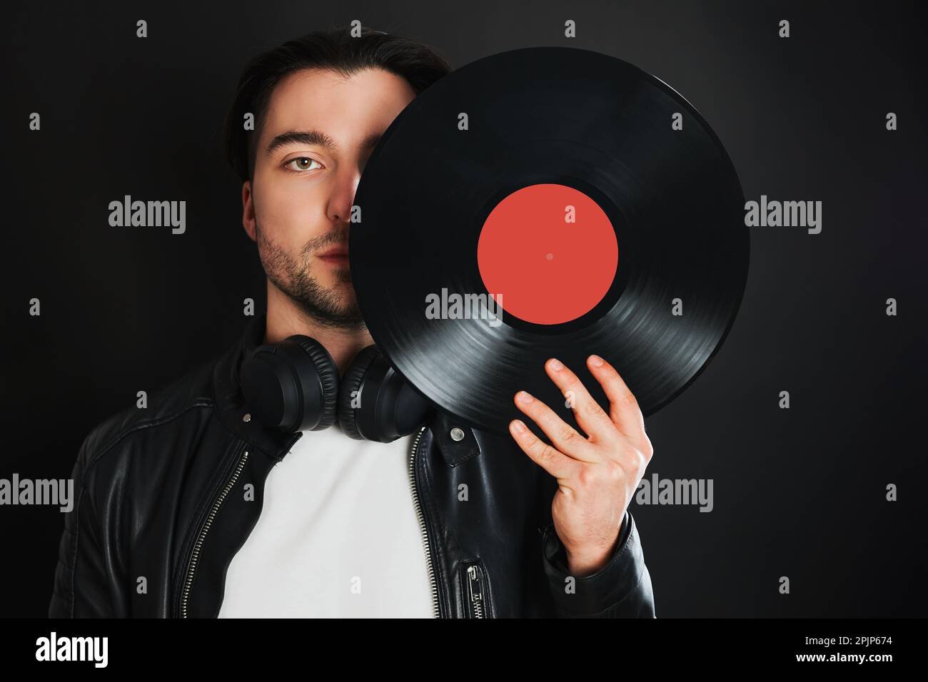 Mann mit Retro-Vinyl-Schallplattenabdeckung. Rock-Style. Klassischer Musikstil. Mann trägt schwarze Jacke mit Vinyl-Schallplatte auf dunklem BA stehen Stockfoto