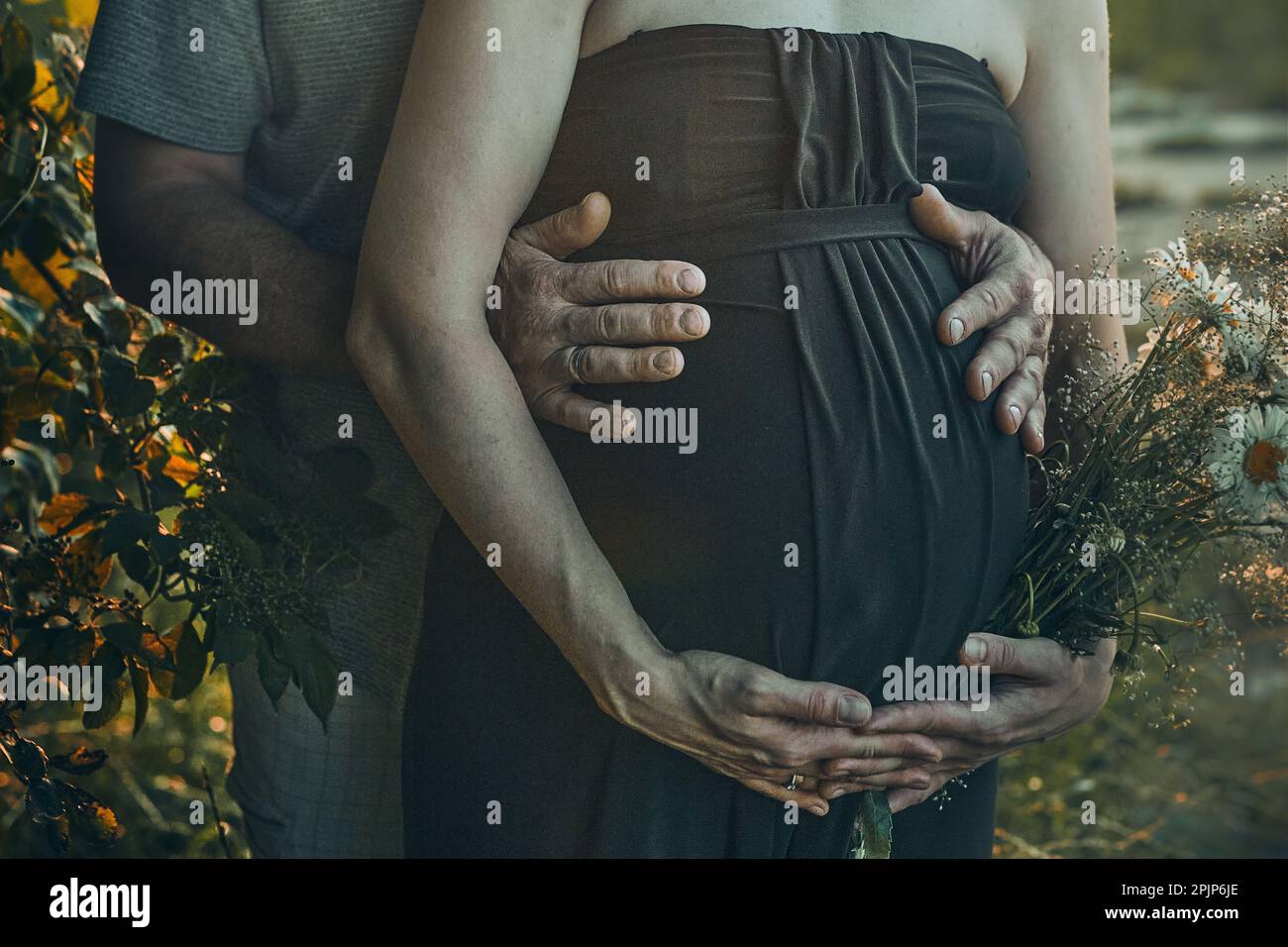 Die Schwangere und ihr Mann umarmen ihren Bauch und stehen im Freien inmitten der Natur. Schwangerschaft, Erwartung, Mutterschaft Konzept Stockfoto