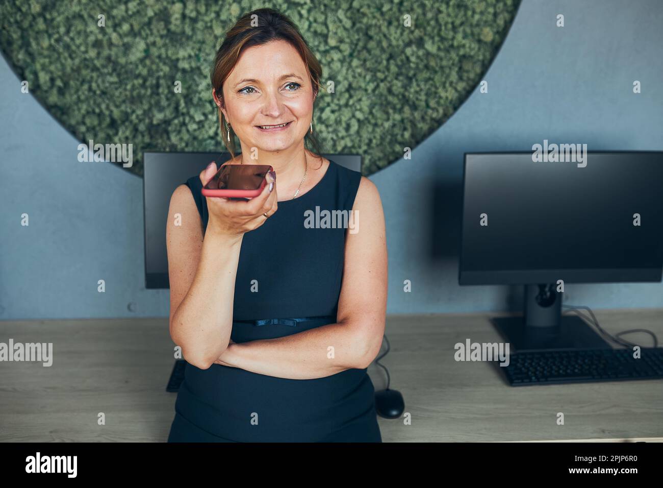 Eine Frau, die geschäftlich im Büro arbeitet. Erwachsene Frau, die mit dem Lautsprechermodus über ein Mobiltelefon spricht. Mit Technologie. Fernkommunikation. Fernsteuerung Stockfoto