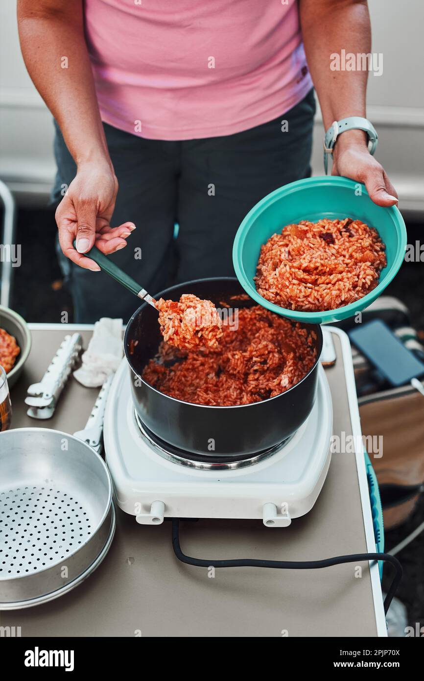 Nahaufnahme von weiblichen Händen, die Reisschale mit Tomatensoße in eine Schüssel legen. Frau kocht Essen auf Elektroherd auf Camping während der Sommerferien Stockfoto