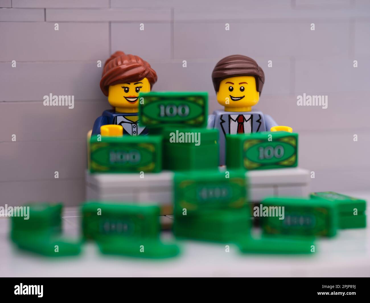 Tambov, Russische Föderation - 25. März 2023 Lego-Geschäftsmann und -Geschäftsfrau-Minifigures sitzen hinter einem Schreibtisch mit einem Haufen Geld drauf. Stockfoto