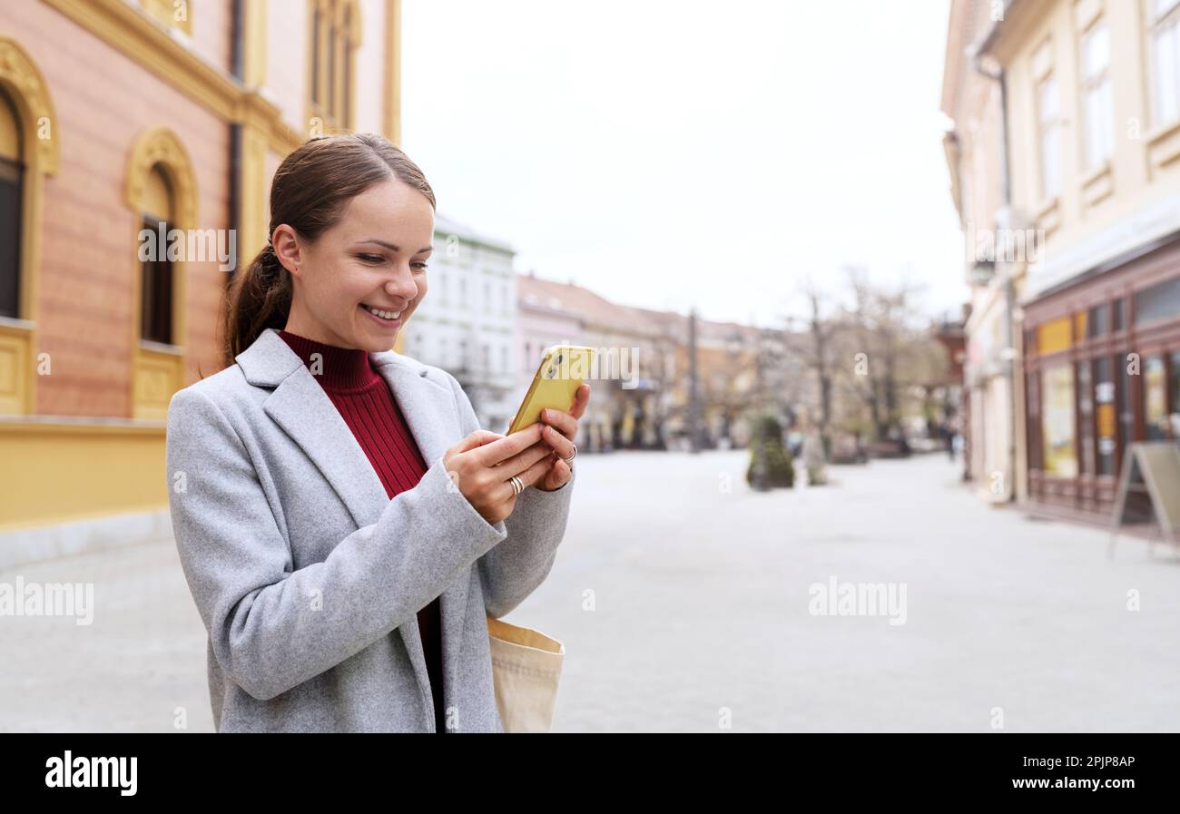 Frau in Freizeitkleidung, die durch die Stadt spaziert und mit ihrem Mobiltelefon online chattet. Stockfoto