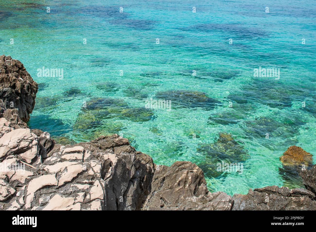 Ein ruhiges türkisfarbenes Gewässer mit einer felsigen Küste im Vordergrund. Stockfoto