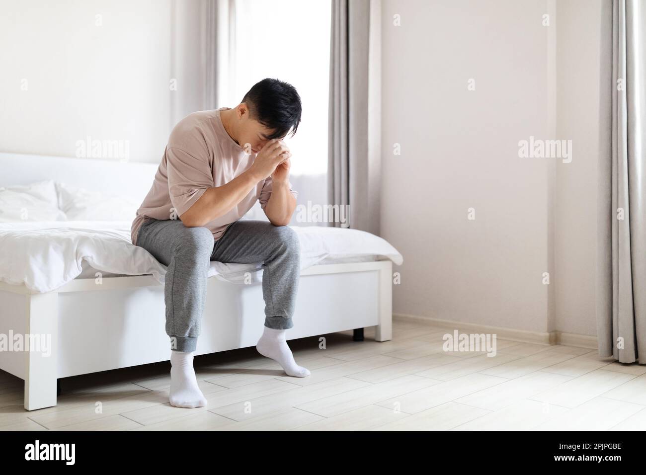 Unglücklicher erwachsener asiatischer Mann, der zu Hause im Bett sitzt Stockfoto