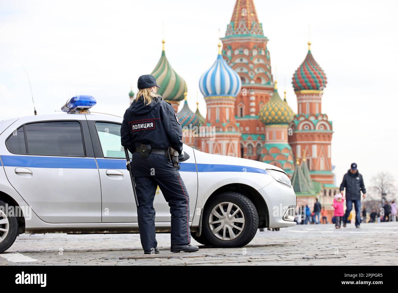 Polizistin patrouilliert im Frühling auf einem Roten Platz in Moskau, der neben dem Auto und der Basilius-Kathedrale steht Stockfoto
