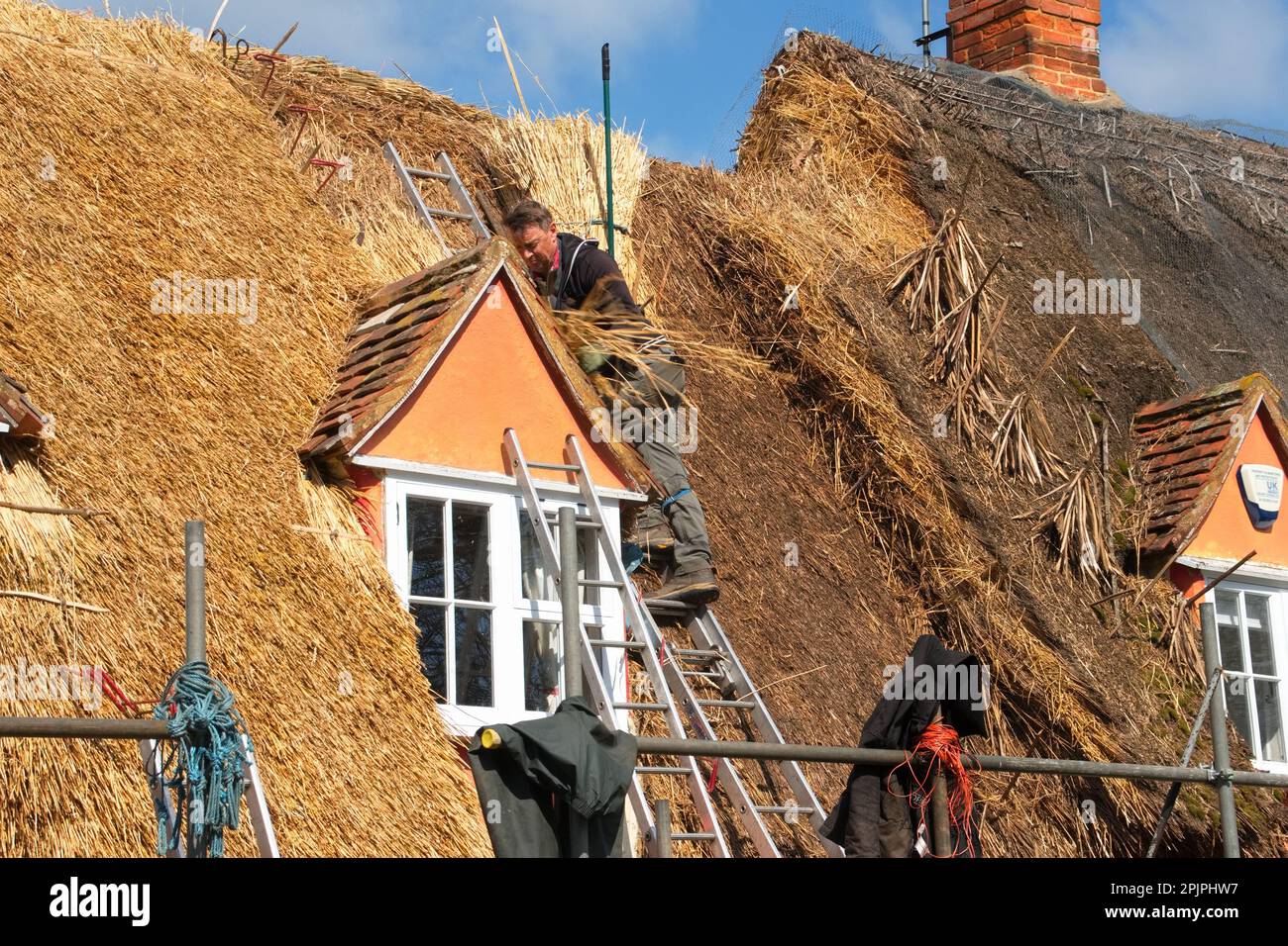 Ein erfahrener Thatcher demonstriert sein Können in einem englischen Cottage, indem er altehrwürdige Techniken verwendet, um das Strohdach zu ersetzen. Stockfoto