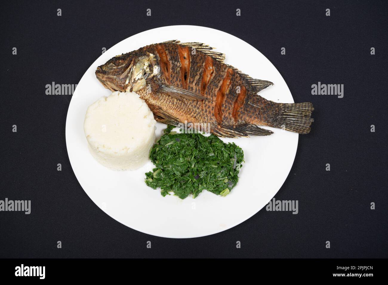 Gegrillter Fisch serviert mit Ugali und Gemüse auf abgelegenem Hintergrund Stockfoto