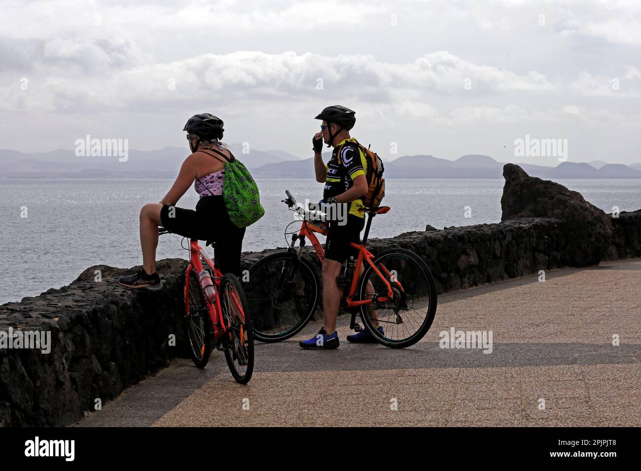 Zwei Radfahrer halten an, um die Aussicht auf dem Küstenpfad von Las Coloradas nach Playa Blanca zu bewundern. Lanzarote-Szene. Februar 2023. Stockfoto