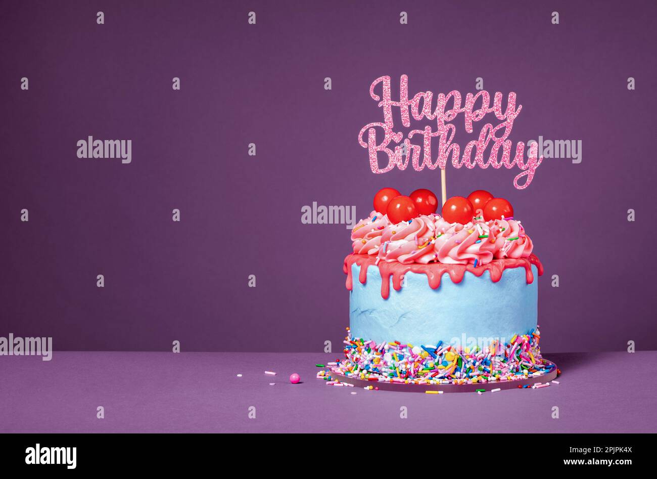Lustiger Tropfkuchen mit roter Ganache, Gummibändern, Streuseln und einem Happy Birthday Topper auf lila Hintergrund. Speicherplatz kopieren. Stockfoto